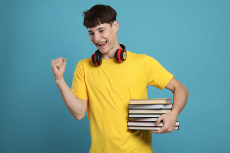 Happy student with books celebrating good exam result on light blue backgroundの写真素材