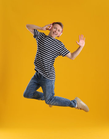 Happy young man with headphones jumping on orange backgroundの写真素材