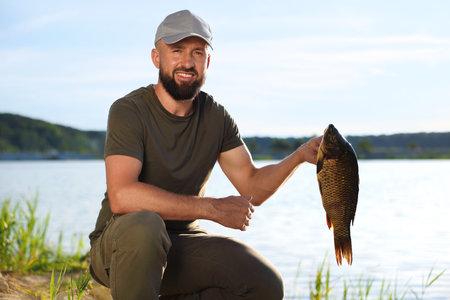 Smiling fisherman holding caught fish near lake at summerの写真素材