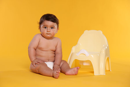 Cute little baby sitting near potty on yellow backgroundの写真素材