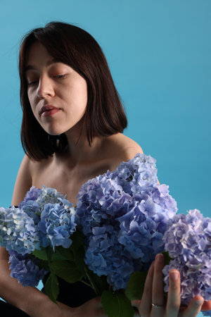 Beautiful young woman with hortensia flowers on light blue backgroundの写真素材