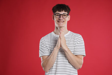 Happy student with clasped hands praying for good exam result on red backgroundの写真素材