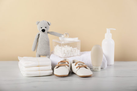 Different baby accessories and toy bear on table against beige background