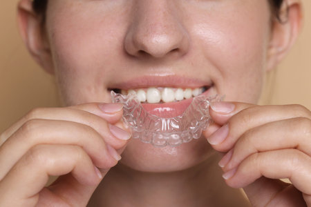 Smiling woman wearing dental aligner on beige background, closeup