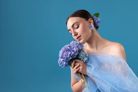 Portrait of beautiful woman with hortensia flowers and cloth on blue background.