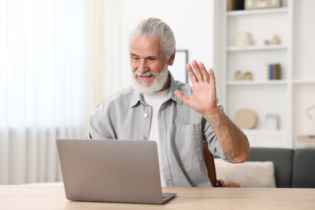 Senior man having online consultation with doctor via laptop at table indoorsの写真素材