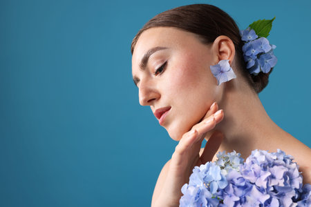 Beautiful young woman with hortensia flowers on blue background. Space for text