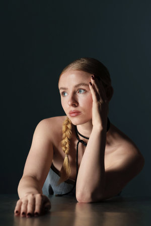 Beautiful woman with pigtail posing at table on dark backgroundの写真素材