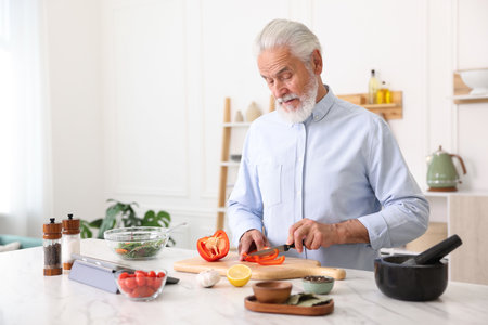 Elderly man cooking at white marble table in kitchenの写真素材