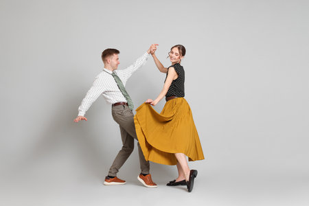Happy couple in retro outfits dancing on light gray backgroundの写真素材