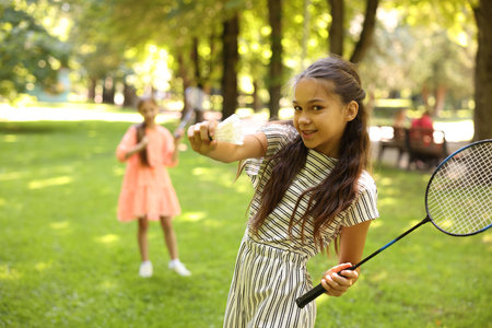 Smiling little girl with badminton racket and shuttlecock playing with her friend in park, selective focusの写真素材