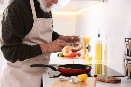 Elderly man cooking dish on cooktop in kitchen, closeupの写真素材