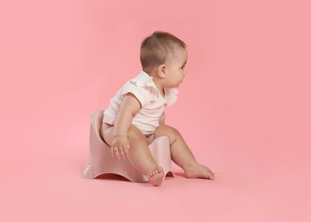 Cute little baby sitting on potty against pink background