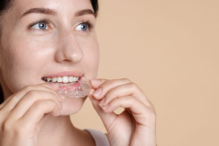 Woman wearing dental aligner on beige background, closeup. Space for text