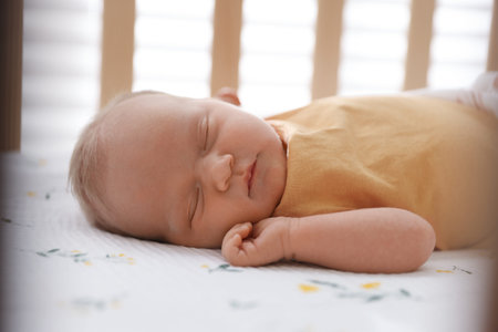 Cute newborn baby lying in crib indoors