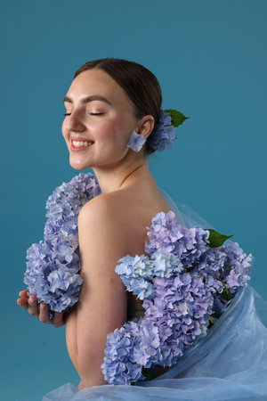 Portrait of beautiful woman with hortensia flowers on blue background