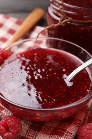 Sweet raspberry jam in glassware and berries on table, closeup