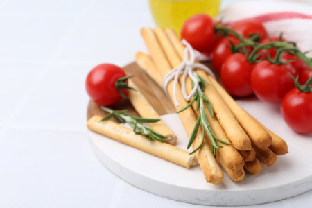 Delicious grissini sticks, rosemary and fresh tomatoes on white table, closeup. Space for textの写真素材