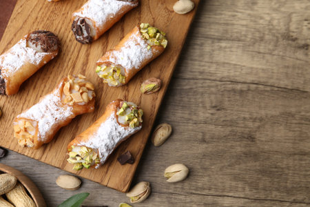 Delicious cannoli with ricotta cheese, peanuts, pistachios, chocolate and powdered sugar on wooden table, flat lay. Space for textの写真素材