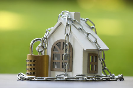 Home security. House model, chain and padlock on light grey table outdoors, closeupの写真素材
