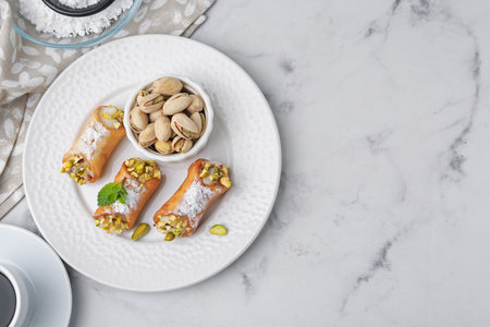 Delicious cannoli with cheese, pistachios, powdered sugar and mint on white marble table, flat lay. Space for textの写真素材