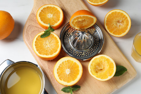 Squeezer with oranges, mint and fresh juice on white table, flat layの写真素材