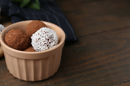 Delicious homemade candies with cocoa powder and coconut flakes in bowl on wooden table, closeup. Space for textの写真素材
