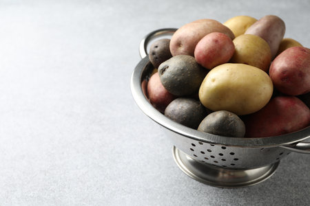 Different types of potatoes in colander on grey table, closeup. Space for textの写真素材