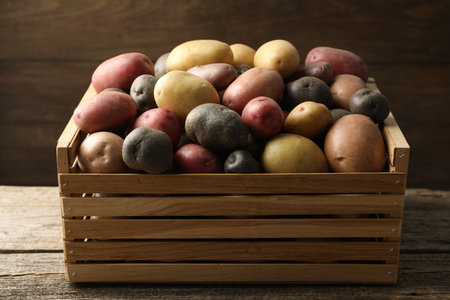 Different types of potatoes in crate on wooden table, closeupの写真素材
