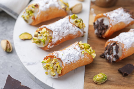 Delicious cannoli with ricotta cheese, pistachios, chocolate and powdered sugar on grey table,...