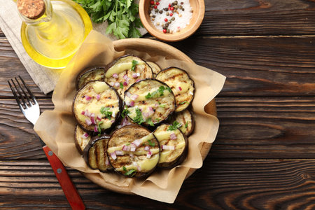 Grilled slices of eggplant with sauce, parsley and onion served on wooden table, flat layの写真素材