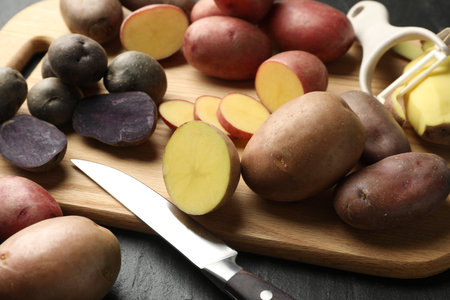 Different types of potatoes, peeler and knife on black table, closeupの写真素材