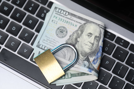 Cyber safety. Metal padlock and dollars on laptop, top viewの写真素材
