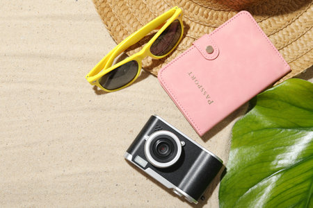 Time for summer vacation. Camera, passport, green leaf and beach accessories on sand, flat lay....