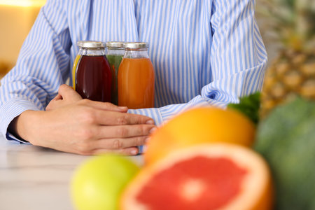 Woman with bottles of tasty juices at light table indoors, selective focusの写真素材