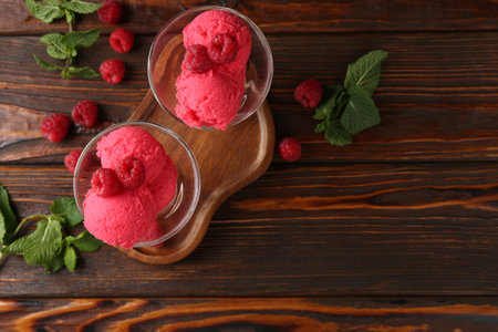 Delicious raspberry sorbet in dessert bowls, mint and fresh berries on wooden table, flat lay. Space for textの写真素材