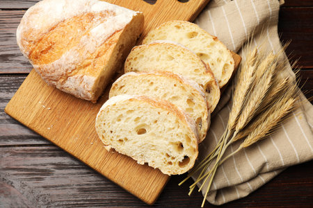 Fresh bread and wheat spikes on wooden table, flat lay