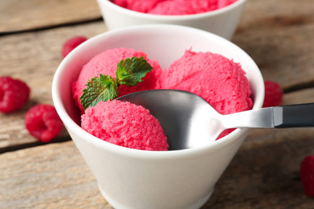 Taking delicious raspberry sorbet with mint from bowl with spoon at wooden table, closeup