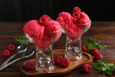 Delicious raspberry sorbet in dessert bowls, mint and fresh berries on wooden table against black background, closeupの写真素材