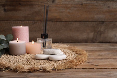 Composition with spa stones, reed air freshener and burning candles on wooden table, closeup. Space for textの写真素材