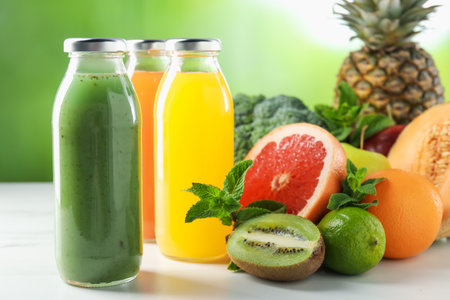 Tasty juices in glass bottles, fresh ingredients and mint on white table against blurred green background, closeupの写真素材