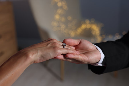 Making marriage proposal. Woman with engagement ring and her fiance holding hands at home, closeup. Bokeh effectの写真素材