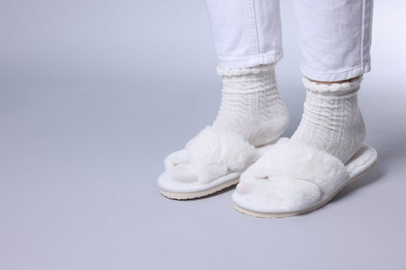Woman in fluffy white slippers on grey background, closeup. Space for text