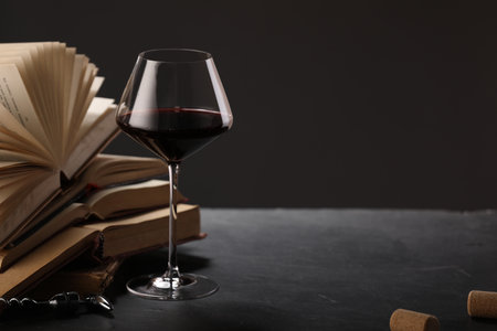 Red wine in glass and books on grey textured table against dark background, closeup. Space for textの写真素材