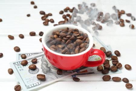 Roasted coffee beans in cup and dollar banknotes on white wooden table, closeupの写真素材
