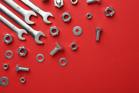 Metal wrenches, nuts and bolts on red background, flat lay. Space for textの写真素材