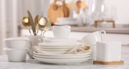 Different clean white dishware, cups and cutlery on marble table indoors