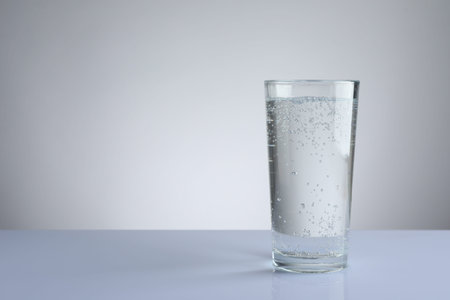 Refreshing soda water in glass on white table against light grey gradient background. Space for text