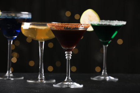 Different martini cocktails in glasses on black table against blurred lights, closeupの写真素材