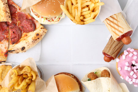 Different delicious fast food on white tiled table, flat lay. Space for text